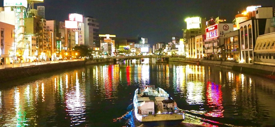 Night view of Nakasu in Fukuoka with neon lights and river cruise boat – a popular nightlife and adult entertainment area in Japan